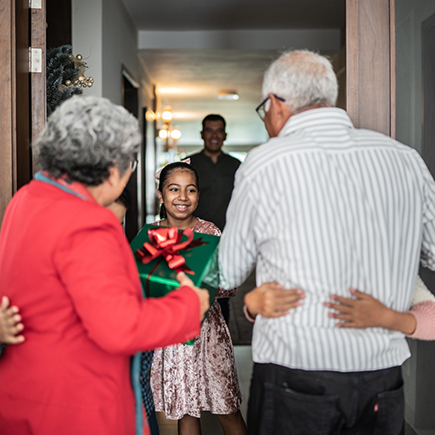 grandparents being welcomed at the door by their grandkids with presents in hand