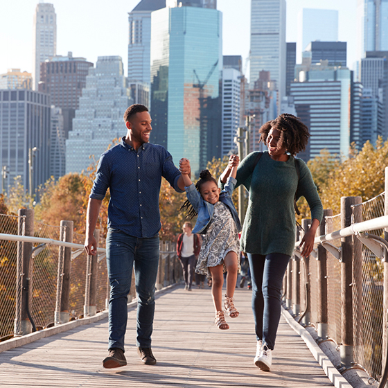 couple with their kid walking on a walk way with a city scape in the background