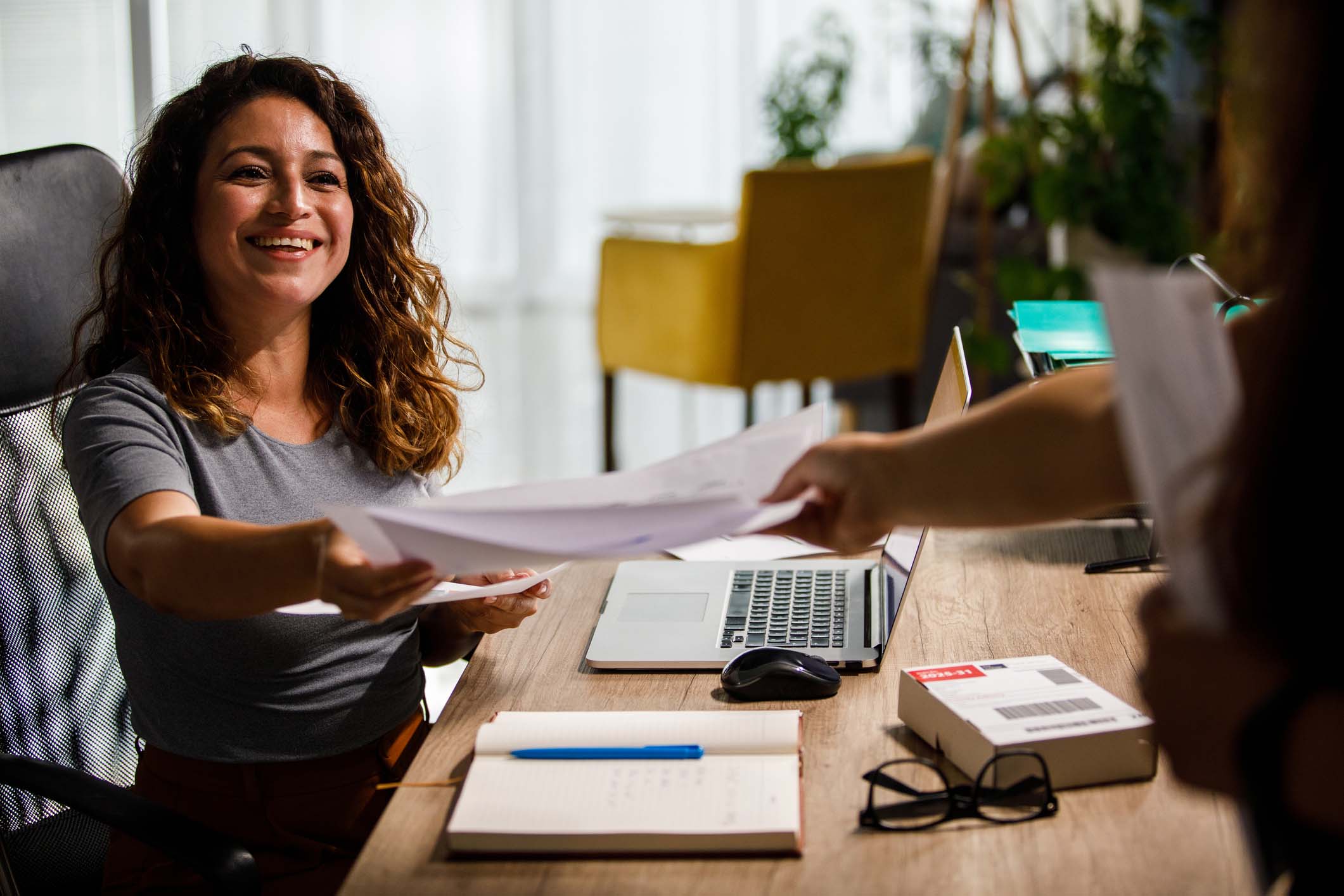 Woman sitting at her desk accepting some paperwork with a smile