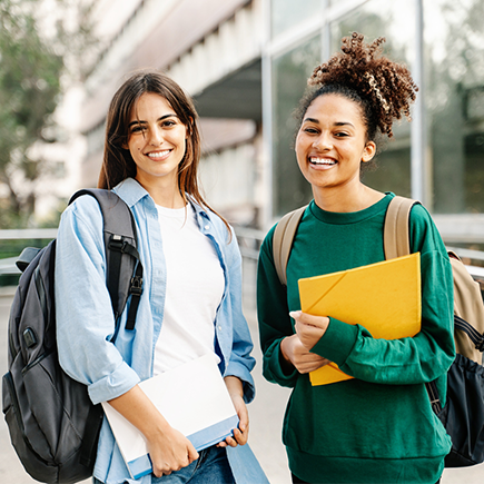 Two students pose for a picture while wearing their backpacks and carrying school supplies