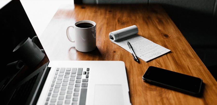 Phone, computer, pen, paper and coffee sitting on a desk