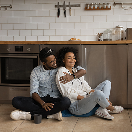Couple sitting on the floor of their kitchen in embrace
