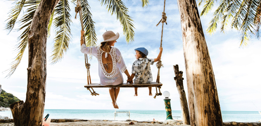 mother and child vacationing, sitting on a swing next to the beach and palm trees